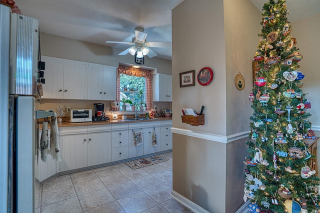 kitchen featuring a textured ceiling, ceiling fan, sink, white fridge, and white cabinetry