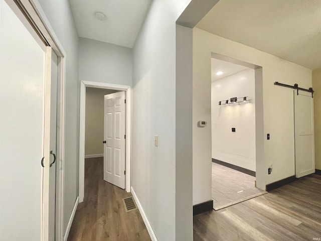 corridor with a barn door and dark hardwood / wood-style flooring