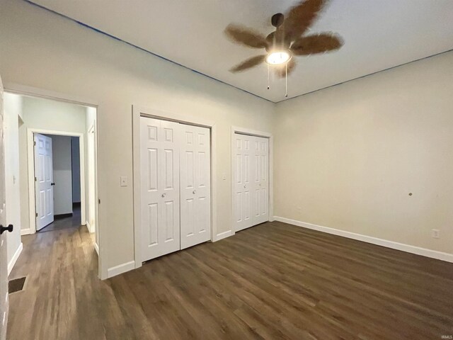 unfurnished bedroom featuring ceiling fan, dark wood-type flooring, and two closets