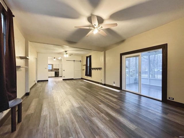 unfurnished living room with hardwood / wood-style floors, a barn door, and ceiling fan