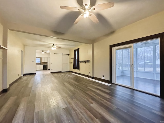 unfurnished living room featuring dark hardwood / wood-style floors, a barn door, and ceiling fan