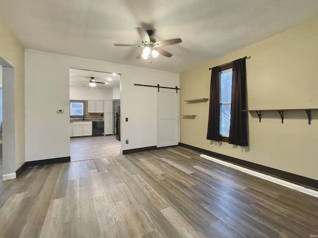 empty room featuring ceiling fan, a barn door, wood-type flooring, and a textured ceiling