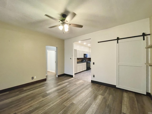 unfurnished living room featuring ceiling fan, a barn door, and dark hardwood / wood-style floors