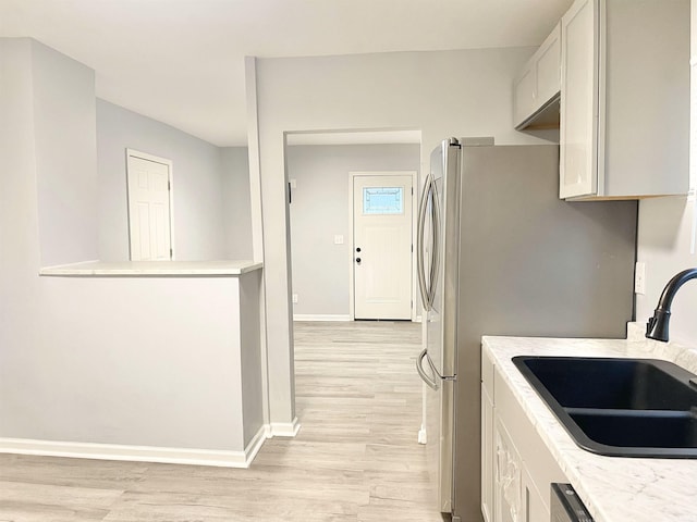 kitchen featuring white cabinetry, sink, dishwasher, stainless steel fridge, and light hardwood / wood-style floors