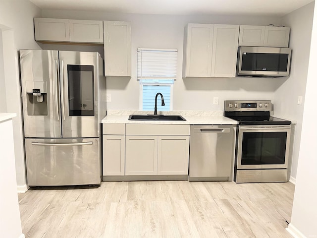 kitchen featuring gray cabinetry, sink, light wood-type flooring, appliances with stainless steel finishes, and light stone counters