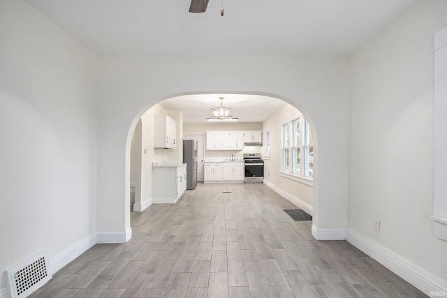 unfurnished living room with ceiling fan with notable chandelier and light hardwood / wood-style flooring