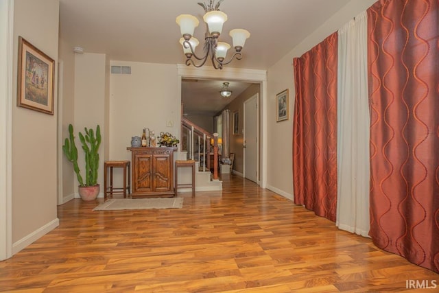 corridor featuring light wood-style flooring, a notable chandelier, visible vents, baseboards, and stairway