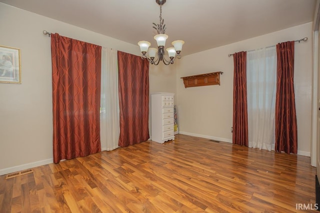 empty room with a chandelier, visible vents, baseboards, and wood finished floors