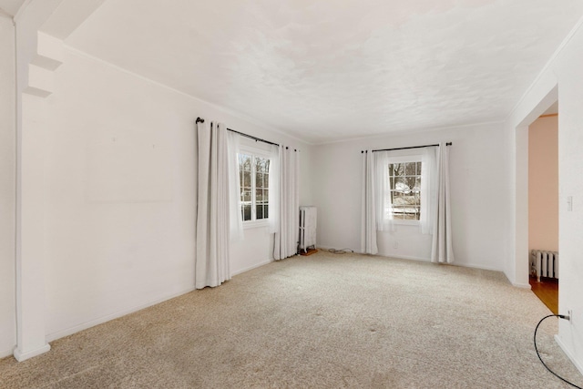 carpeted empty room featuring crown molding, radiator, and a healthy amount of sunlight