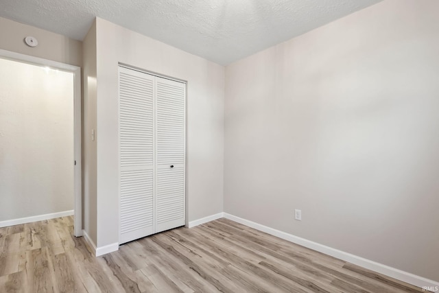 unfurnished bedroom featuring a closet, a textured ceiling, and light wood-type flooring