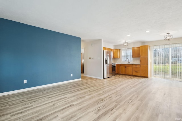 kitchen with appliances with stainless steel finishes, light hardwood / wood-style flooring, pendant lighting, and sink