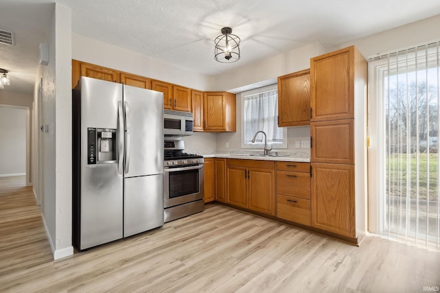 kitchen featuring a wealth of natural light, sink, stainless steel appliances, pendant lighting, and light hardwood / wood-style floors