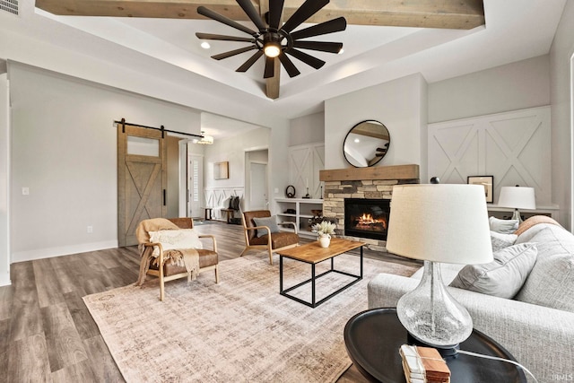 living room featuring a raised ceiling, a barn door, ceiling fan, and wood-type flooring