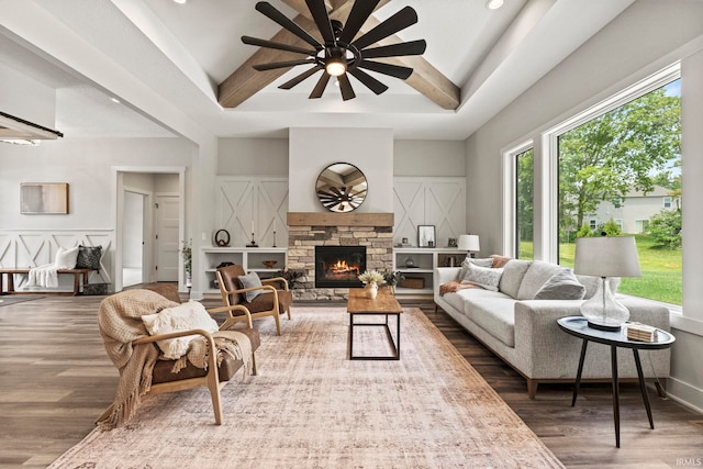 living room with ceiling fan, beam ceiling, a fireplace, and dark wood-type flooring