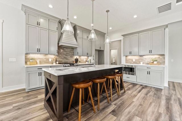 kitchen with gray cabinetry, a center island with sink, custom range hood, and sink