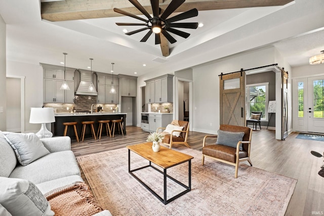 living room featuring a barn door, a tray ceiling, ceiling fan, and hardwood / wood-style flooring