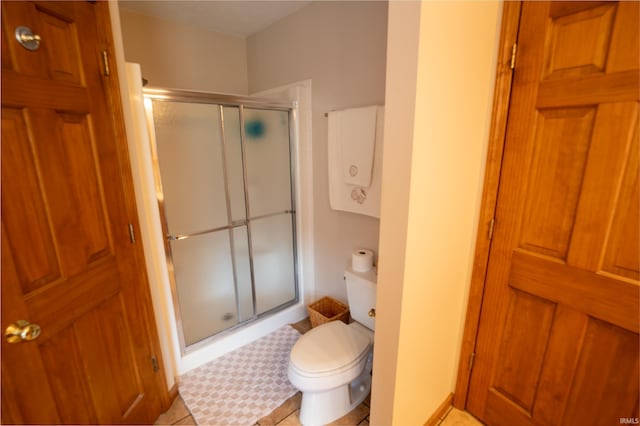 bathroom featuring tile patterned flooring, toilet, and a shower with door