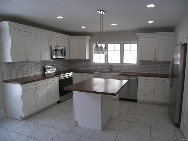 kitchen with sink, hanging light fixtures, stainless steel appliances, wooden counters, and a kitchen island