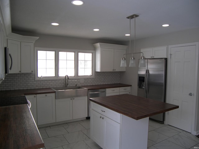 kitchen with wood counters, stainless steel appliances, a kitchen island, decorative light fixtures, and white cabinetry