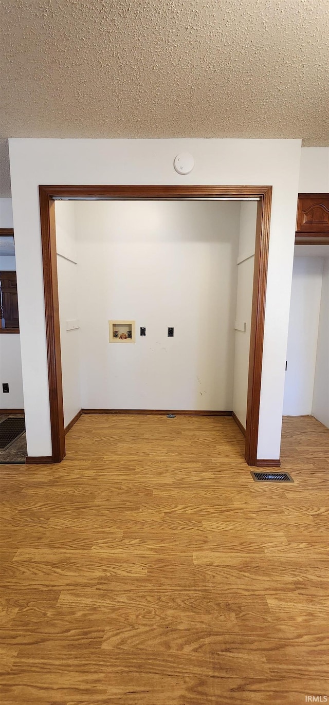 clothes washing area with light hardwood / wood-style flooring, washer hookup, and a textured ceiling