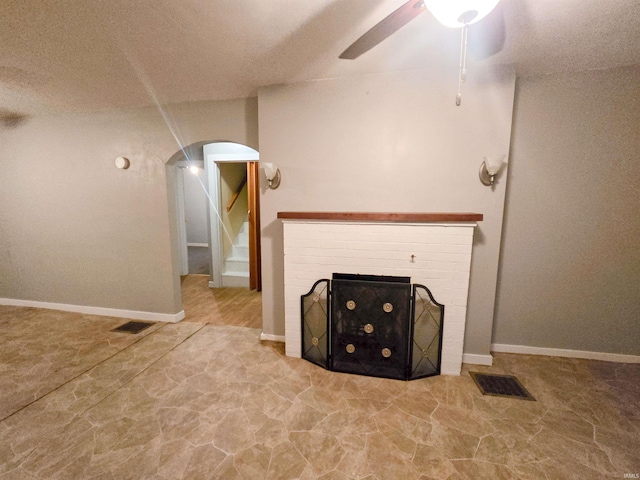 unfurnished living room featuring ceiling fan and a brick fireplace