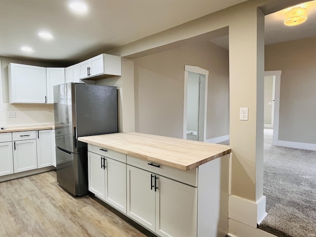 kitchen with decorative backsplash, stainless steel fridge, white cabinetry, light colored carpet, and butcher block counters