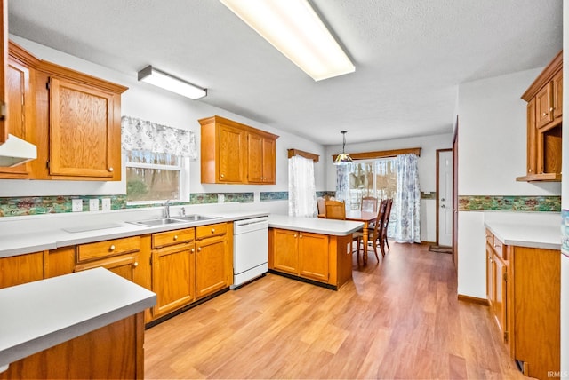 kitchen featuring pendant lighting, white dishwasher, sink, light hardwood / wood-style floors, and kitchen peninsula