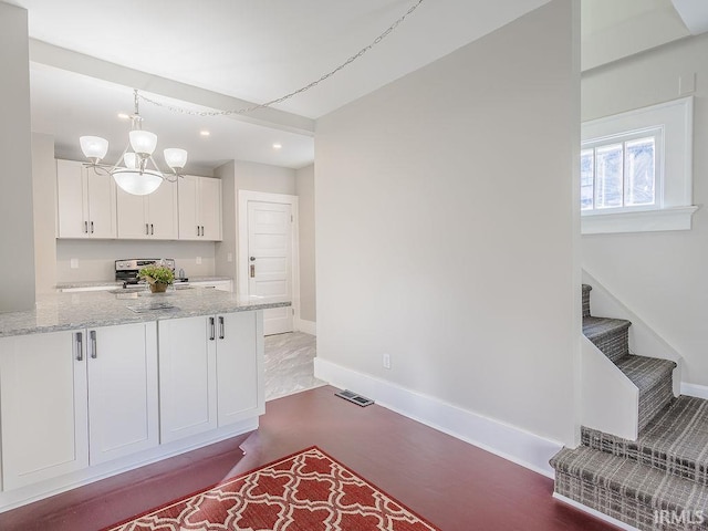 kitchen with light stone countertops, stainless steel electric stove, decorative light fixtures, a notable chandelier, and white cabinets