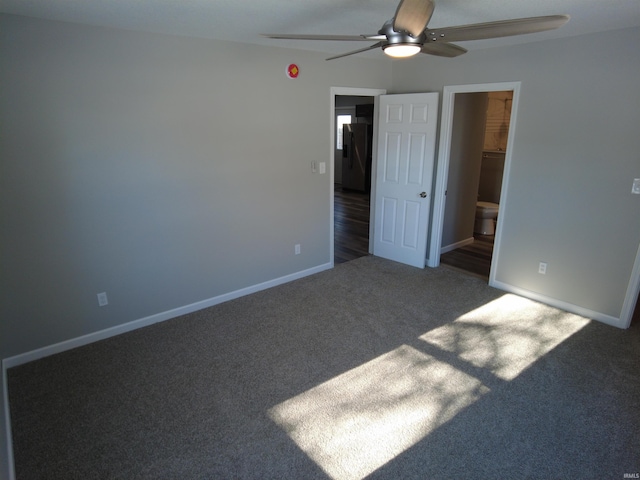 unfurnished bedroom with ceiling fan, black fridge, a walk in closet, a closet, and dark carpet