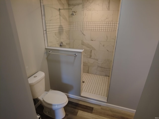 bathroom featuring toilet, a tile shower, and wood-type flooring