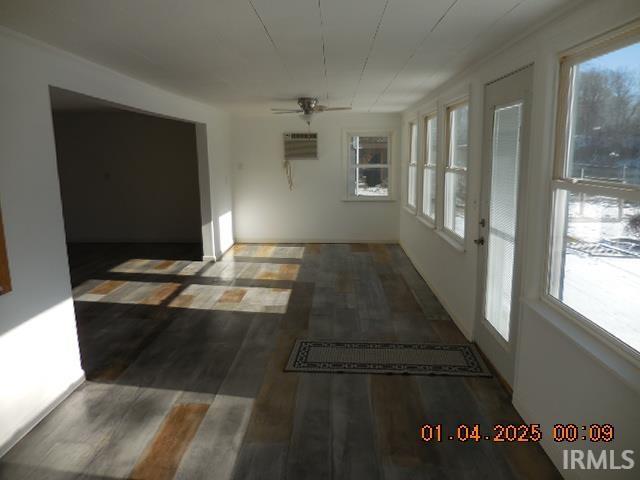 interior space with a wall unit AC, a wealth of natural light, ceiling fan, and dark hardwood / wood-style floors