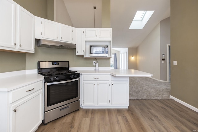 kitchen featuring kitchen peninsula, vaulted ceiling with skylight, white cabinetry, and stainless steel gas range