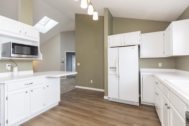 kitchen featuring white cabinetry, stainless steel microwave, white fridge with ice dispenser, and lofted ceiling with skylight