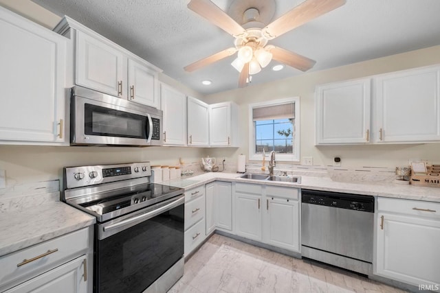 kitchen featuring appliances with stainless steel finishes, light stone counters, ceiling fan, sink, and white cabinetry