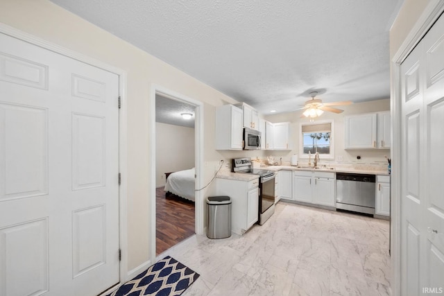 kitchen featuring appliances with stainless steel finishes, a textured ceiling, ceiling fan, sink, and white cabinetry