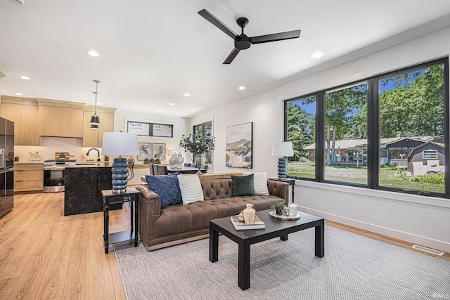 living room with light wood-type flooring, ceiling fan, and sink