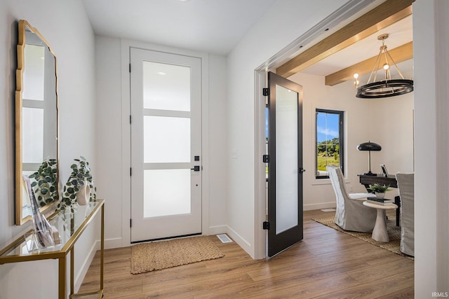 foyer featuring hardwood / wood-style flooring, plenty of natural light, beamed ceiling, and an inviting chandelier