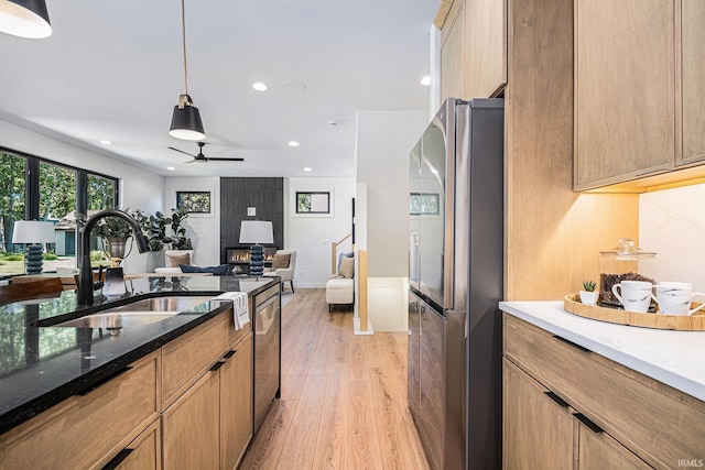 kitchen with light hardwood / wood-style flooring, ceiling fan, dark stone countertops, appliances with stainless steel finishes, and decorative light fixtures