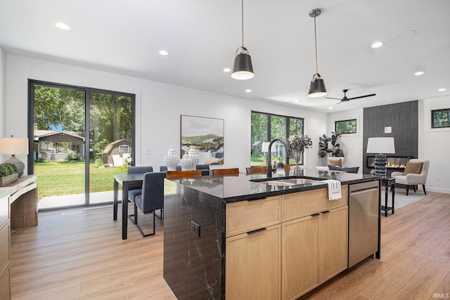 kitchen featuring dishwasher, light brown cabinets, dark stone counters, a center island with sink, and sink