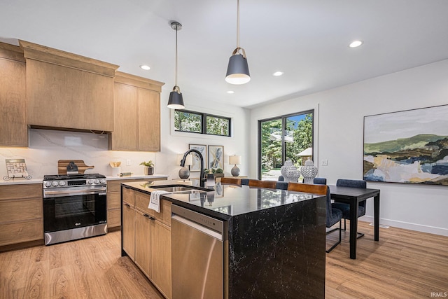 kitchen with sink, hanging light fixtures, stainless steel appliances, an island with sink, and light hardwood / wood-style floors