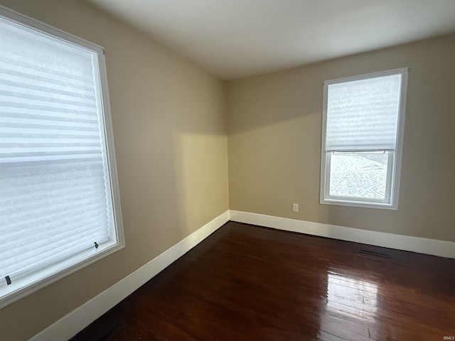 empty room with dark wood-style flooring, visible vents, and baseboards