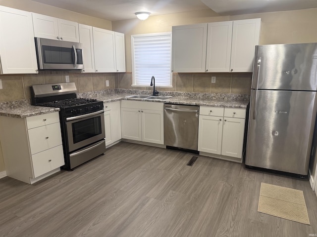 kitchen with stainless steel appliances, decorative backsplash, light wood-style floors, white cabinets, and a sink