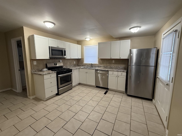 kitchen featuring a sink, light stone countertops, stainless steel appliances, white cabinetry, and backsplash