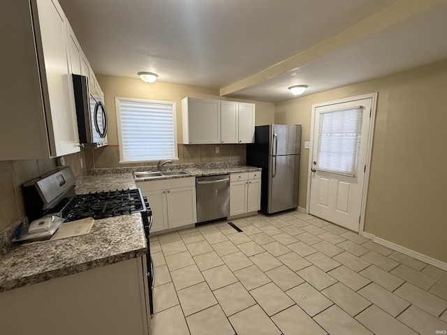 kitchen featuring baseboards, decorative backsplash, stainless steel appliances, white cabinetry, and a sink