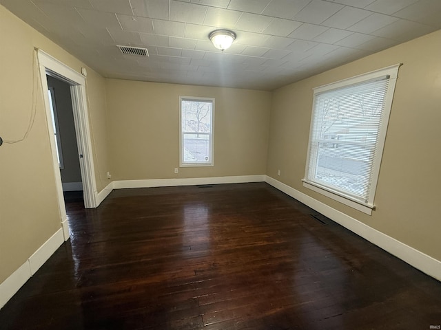 unfurnished room featuring dark wood-type flooring, visible vents, and baseboards