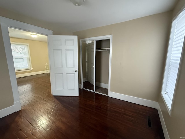 unfurnished bedroom with visible vents, a closet, baseboards, and dark wood-type flooring