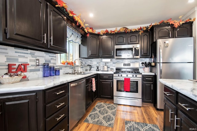 kitchen with light stone countertops, sink, stainless steel appliances, backsplash, and light hardwood / wood-style floors