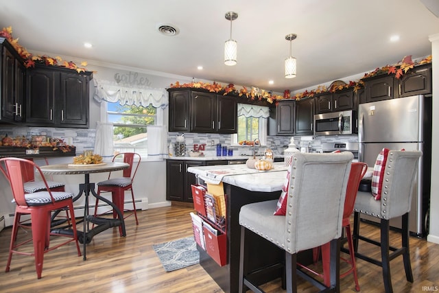 kitchen with a kitchen bar, light wood-type flooring, ornamental molding, stainless steel appliances, and a kitchen island