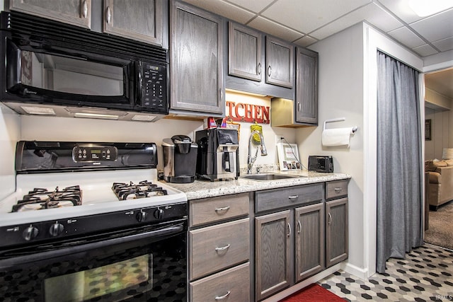 kitchen with a drop ceiling, gas range gas stove, dark brown cabinets, sink, and light tile patterned floors