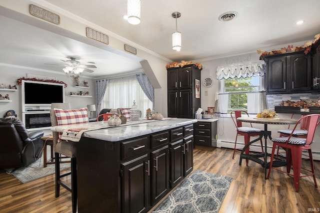 kitchen featuring a center island, dark wood-type flooring, a kitchen breakfast bar, hanging light fixtures, and ornamental molding